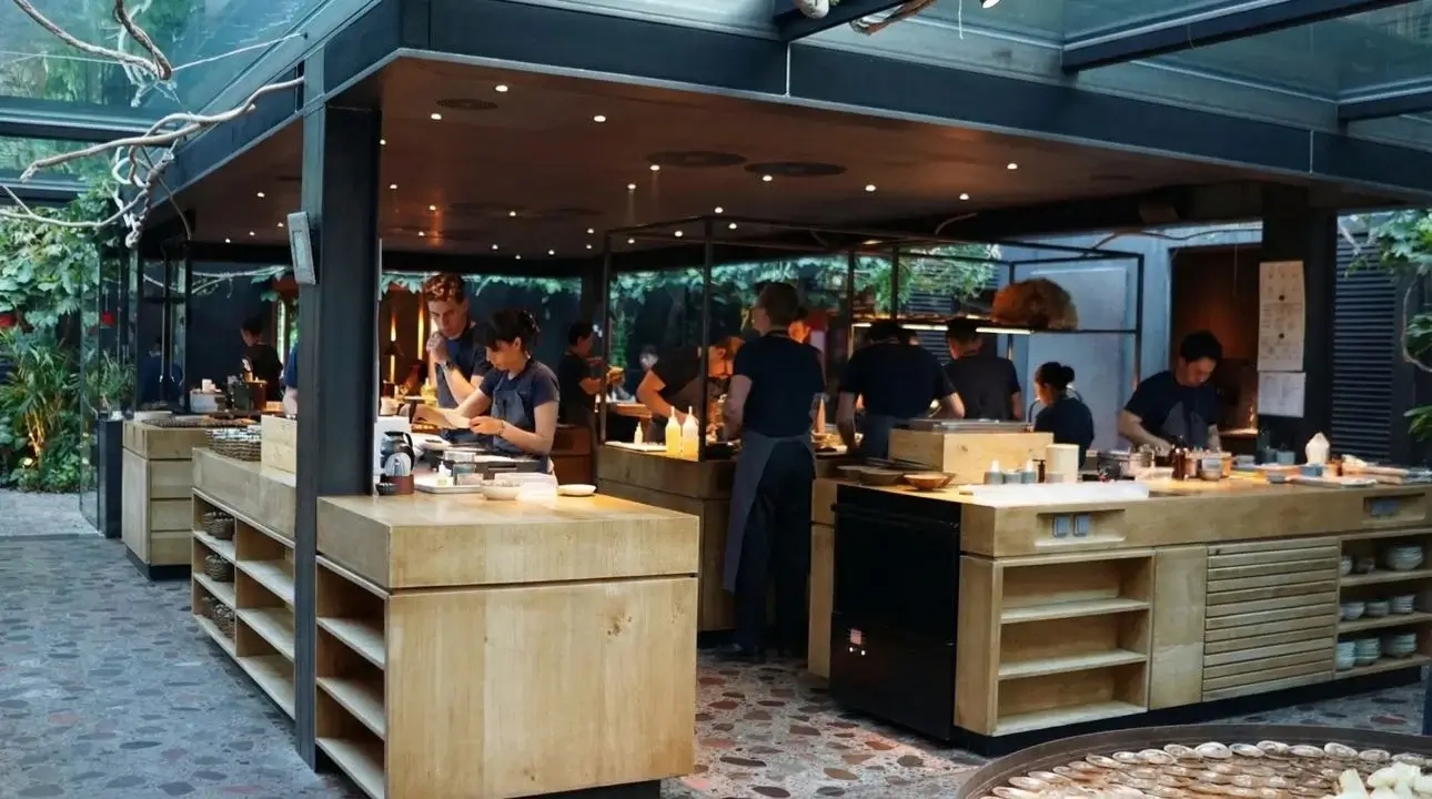 Fjeld's open kitchen with chefs preparing dishes at wooden counters, natural light streaming through large windows